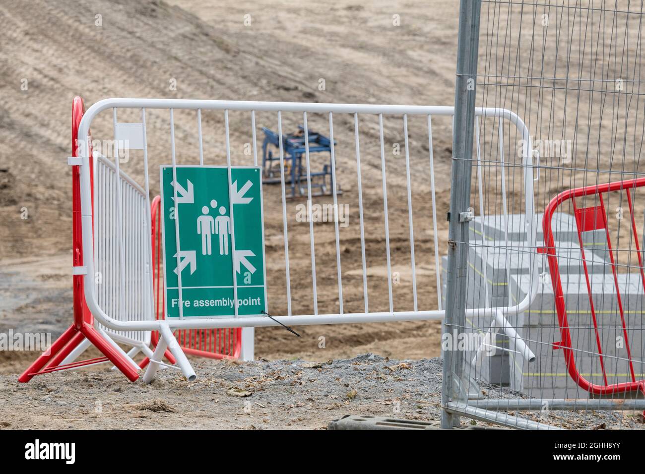 Cartello verde del punto di assemblaggio antincendio sulla recinzione della barriera del cantiere. Per la salute e la sicurezza sul lavoro, vigili del fuoco Regno Unito, cosa fare in caso di incendio. Foto Stock