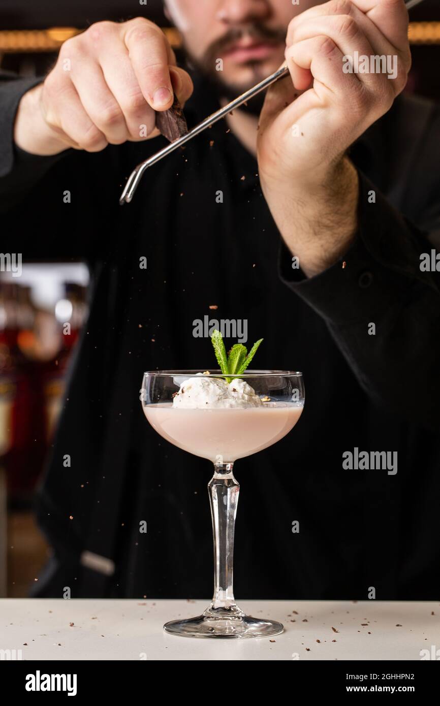 Il barista maschio ruba il cioccolato con un grater su un cocktail con gelato e Baileys in un bicchiere sul Foto Stock