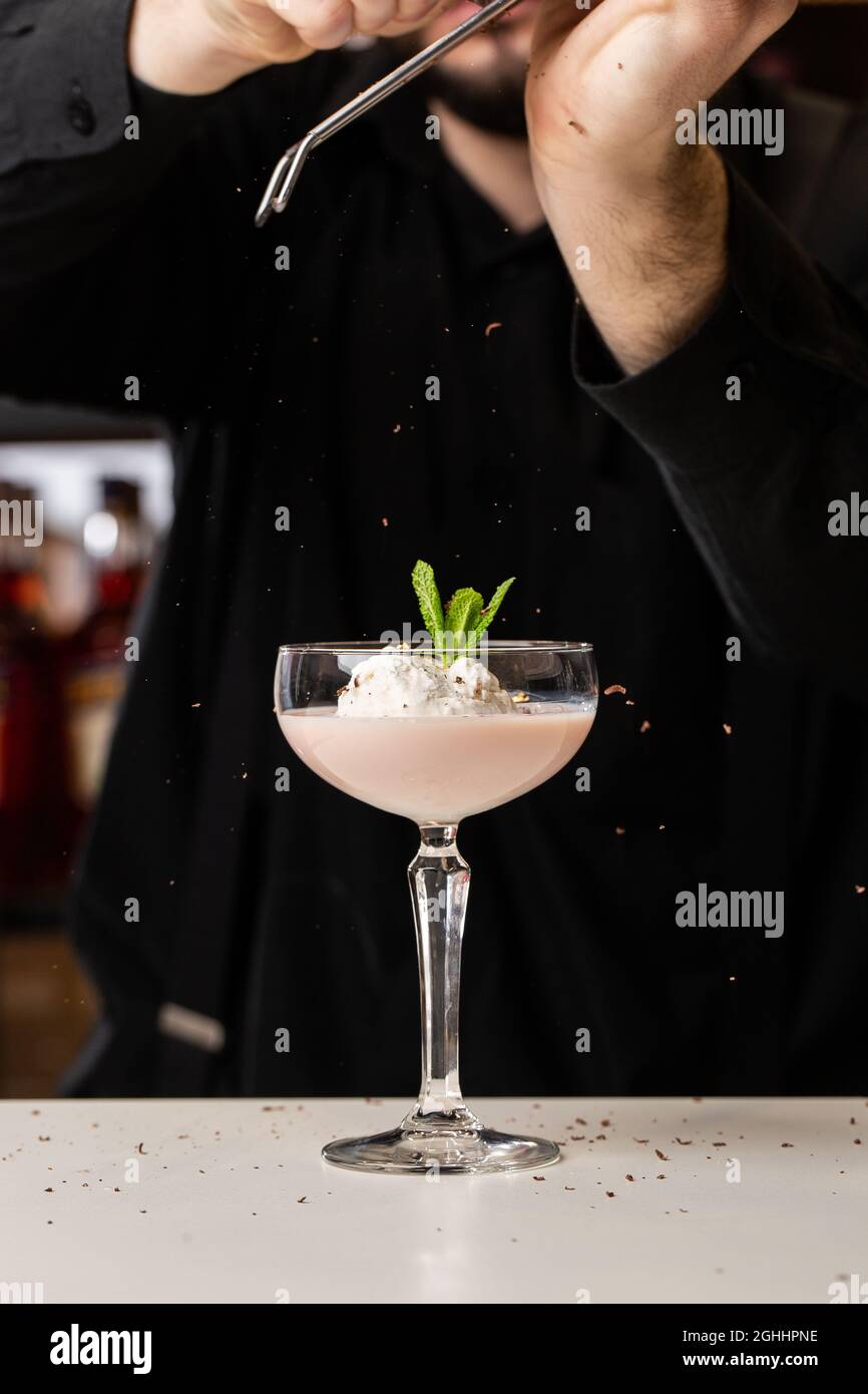 Il barista maschio ruba il cioccolato con un grater su un cocktail con gelato e Baileys in un bicchiere sul Foto Stock