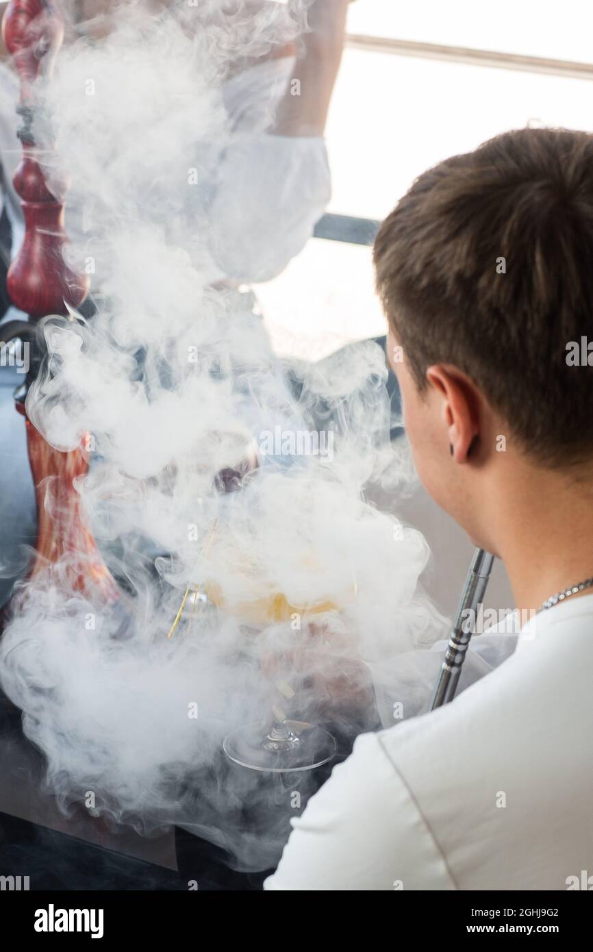 Primo piano dell'uomo che fuma il tubo di hookah tradizionale. Uomo che esala il fumo. Hookah e scintille da carboni. Narghilè, scintille, scintille di hookah. Foto Stock