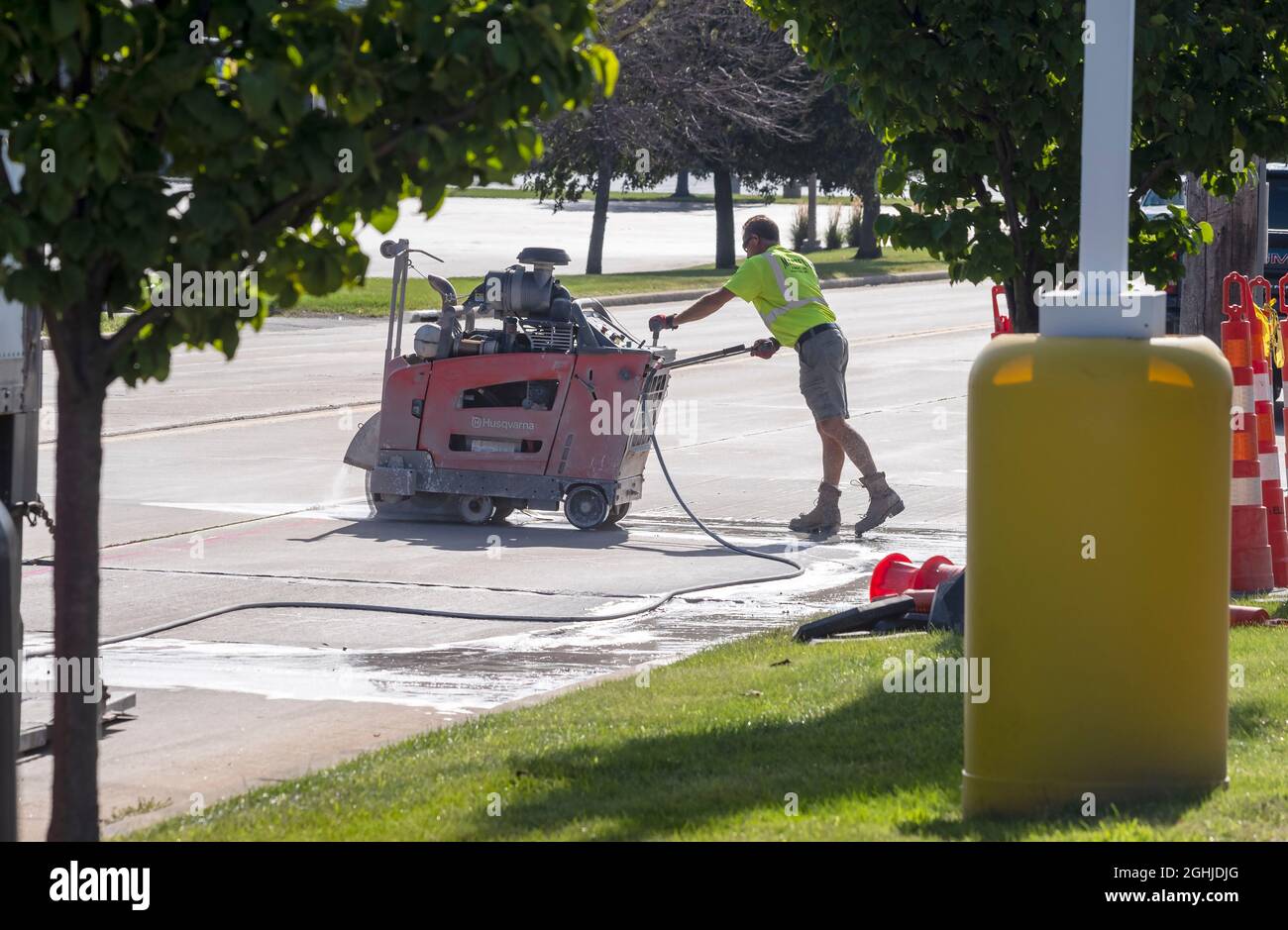Operatore di costruzione stradale che taglia una sezione di pavimentazione stradale con una sega di calcestruzzo. Foto Stock