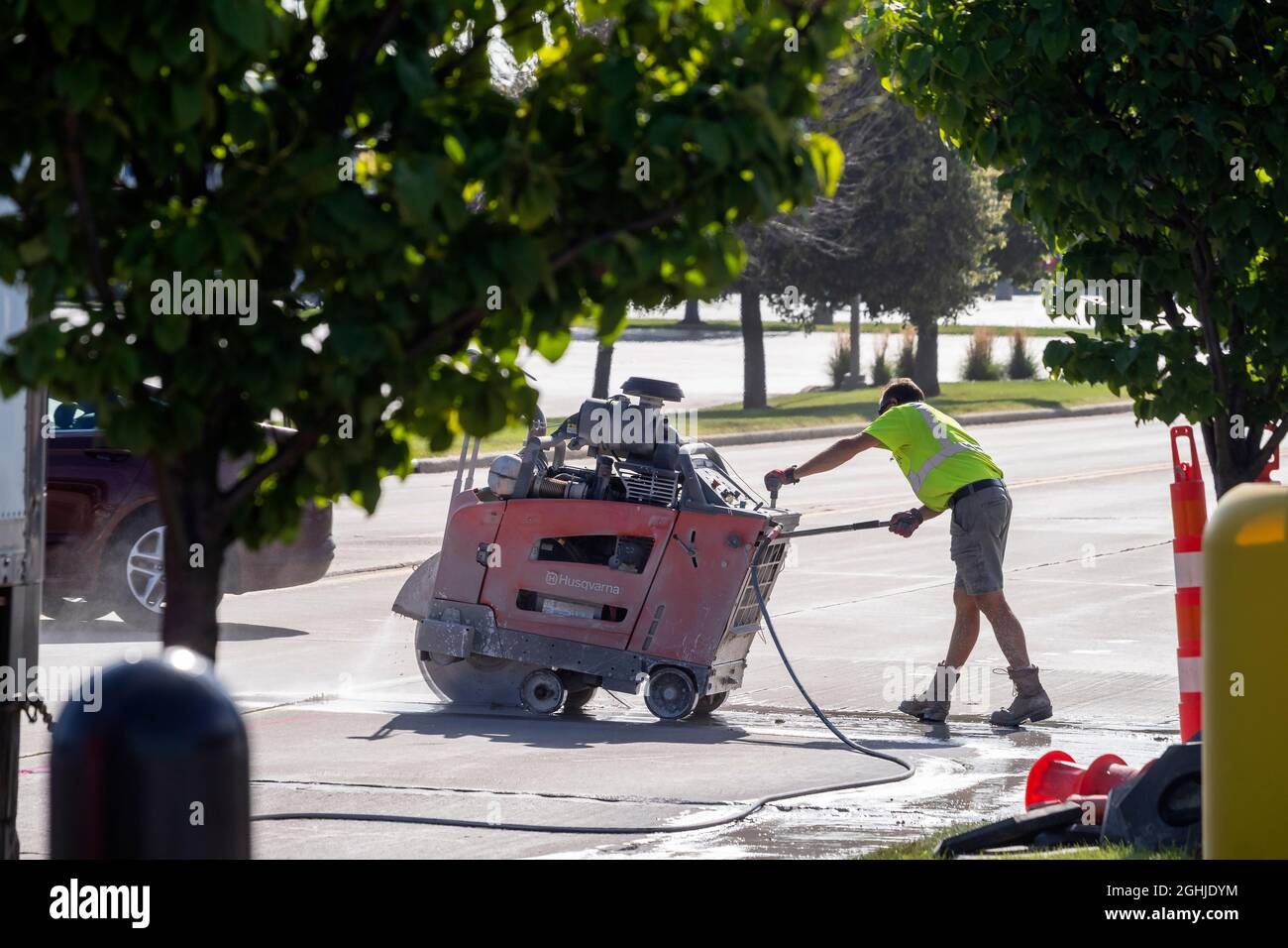 Operatore di costruzione stradale che taglia una sezione di pavimentazione stradale con una sega di calcestruzzo. Foto Stock