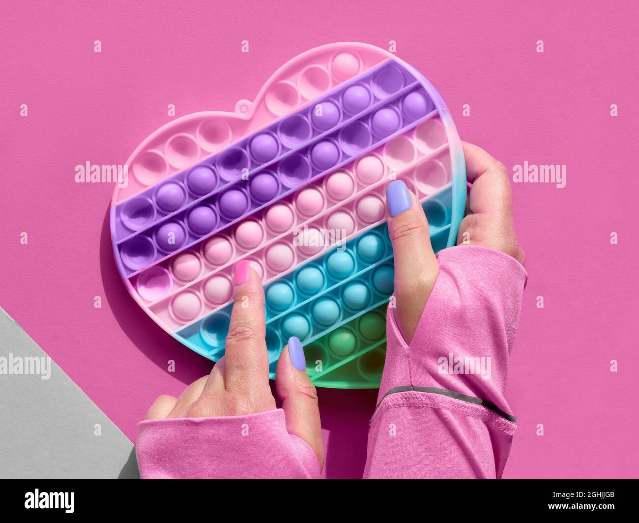 Cuore a forma di papa esso antistress giocattolo con mano femminile. Semplice fodget sensoriale a concavità nei colori di LGBT. Piatto posare su carta rosa, composizione quadrata. Aiuto Foto Stock