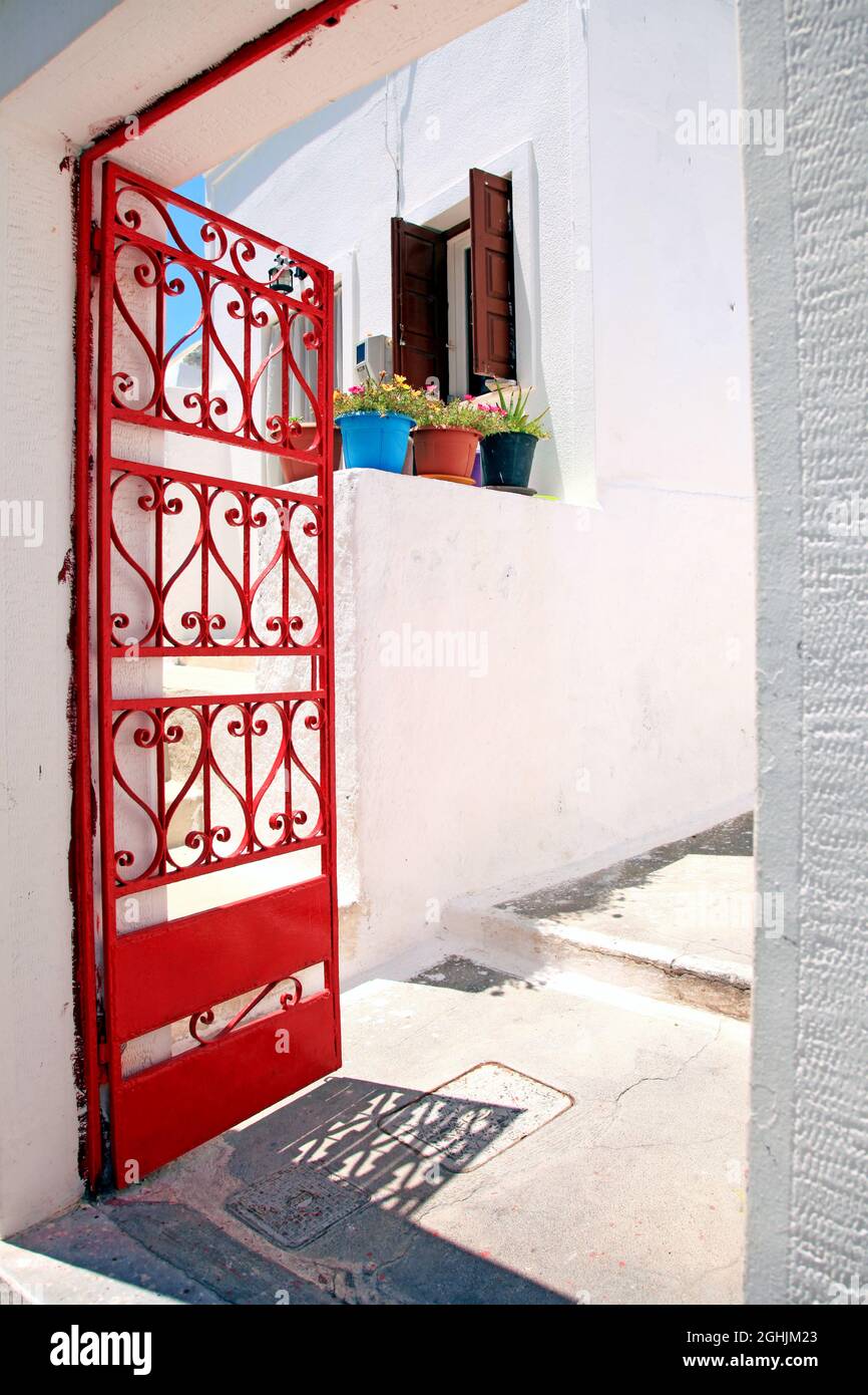 Un cancello rosso e vasi di fiori su un muro nel villaggio tradizionale di Megalochori a Santorini, in Grecia. Foto Stock