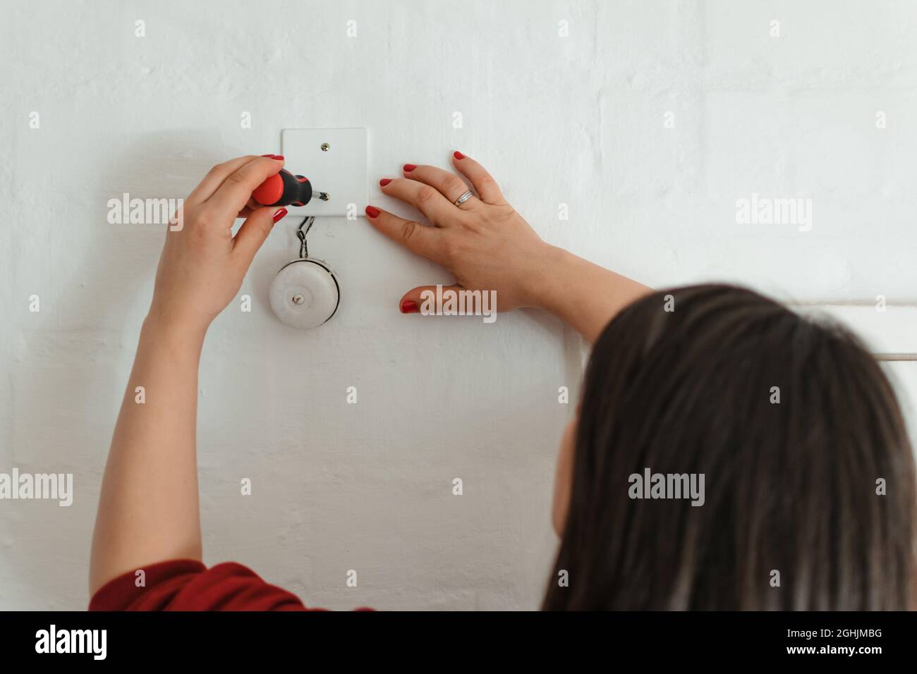 Primo piano di una donna con unghie dipinte riparando un campanello con un cacciavite Foto Stock