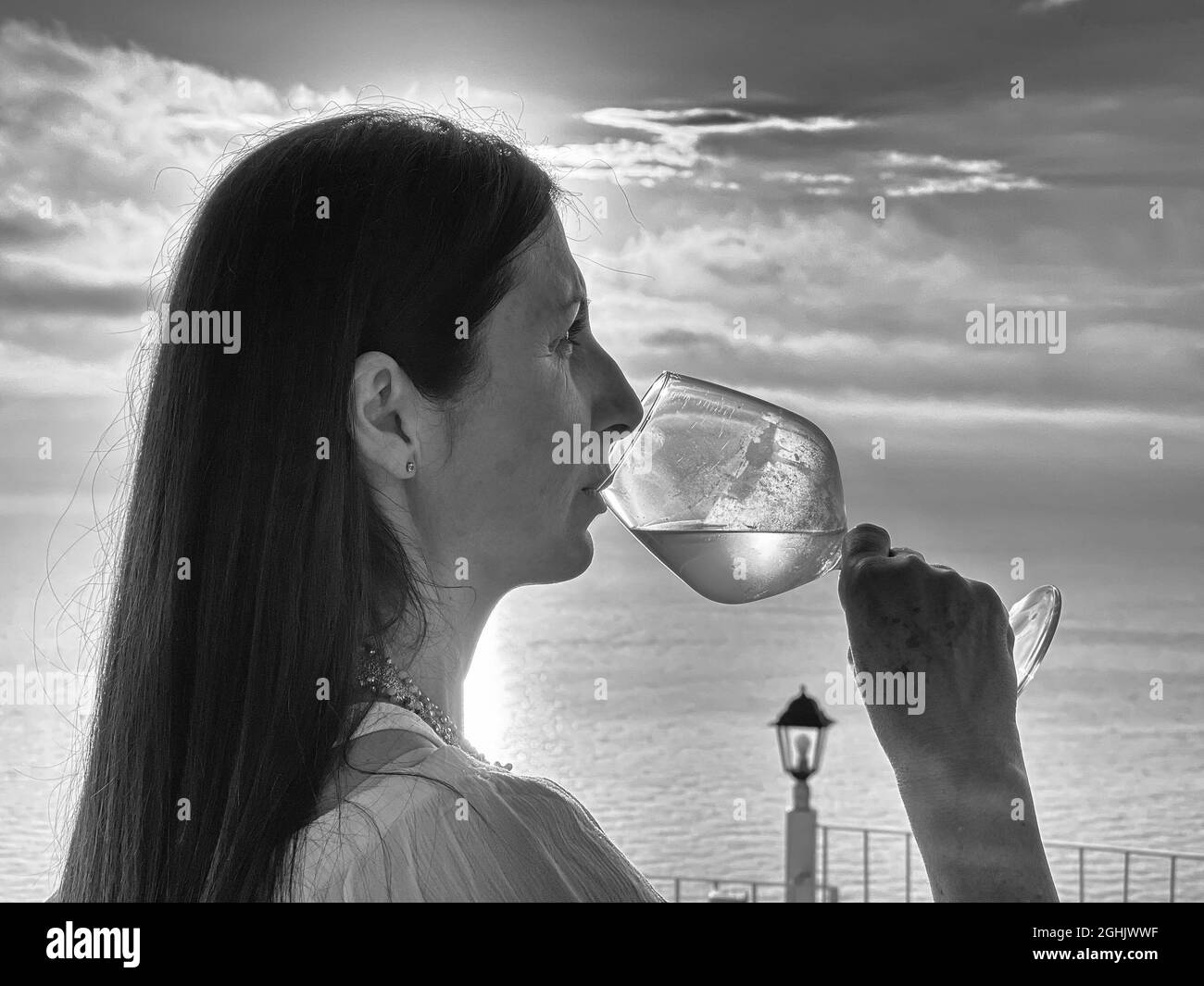 Foto in scala di grigi di una donna di mezza età dall'Italia che beve vino godendosi la sua vacanza sulla spiaggia Foto Stock