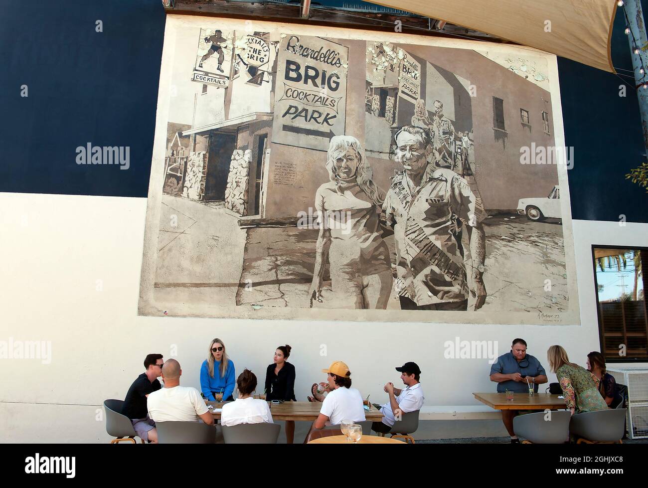 Giovani patroni che si godono un drink sul patio del Brig di Brandelli sotto un murale classico dipinto da Art Mortimer su Abate Kinney Blvd. A Venezia, CA Foto Stock