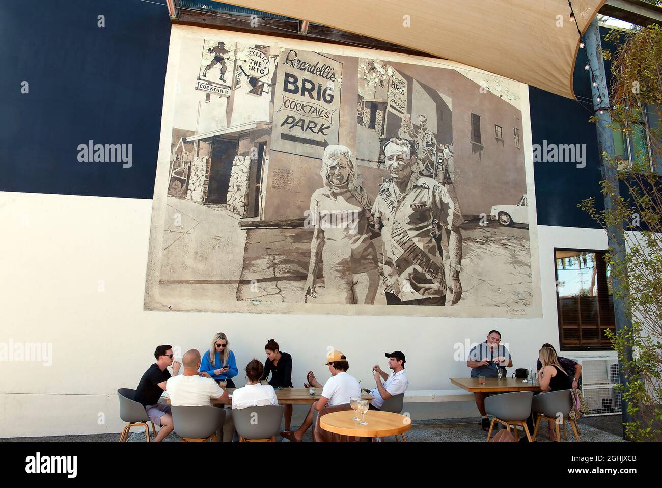 Giovani patroni che si godono un drink sul patio del Brig di Brandelli sotto un murale classico dipinto da Art Mortimer su Abate Kinney Blvd. A Venezia, CA Foto Stock