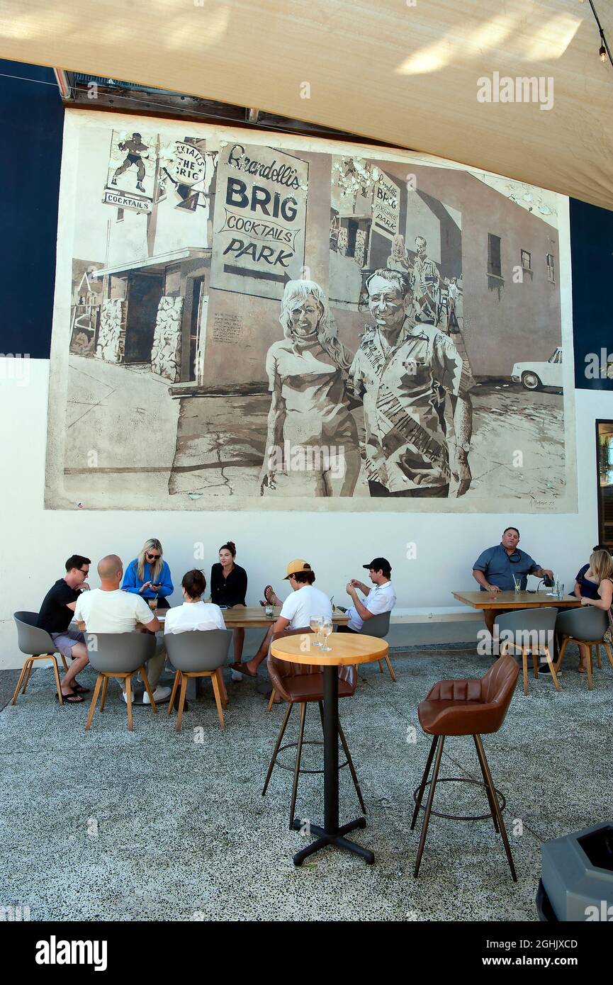 Giovani patroni che si godono un drink sul patio del Brig di Brandelli sotto un murale classico dipinto da Art Mortimer su Abate Kinney Blvd. A Venezia, CA Foto Stock