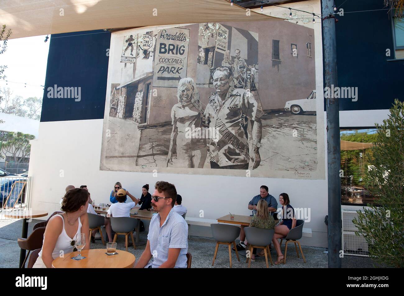 Giovani patroni che si godono un drink sul patio del Brig di Brandelli sotto un murale classico dipinto da Art Mortimer su Abate Kinney Blvd. A Venezia, CA Foto Stock