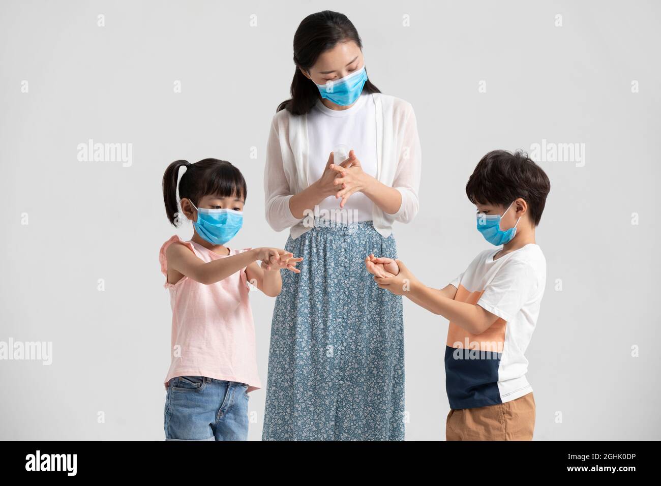 Bambini che usano l'igienizzatore per le mani con l'aiuto della madre Foto Stock