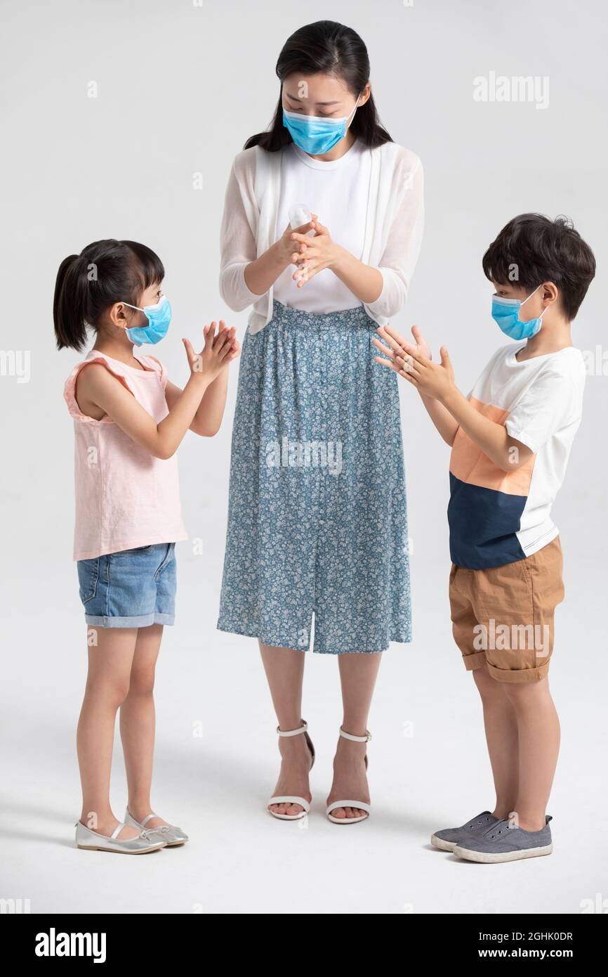 Bambini che usano l'igienizzatore per le mani con l'aiuto della madre Foto Stock