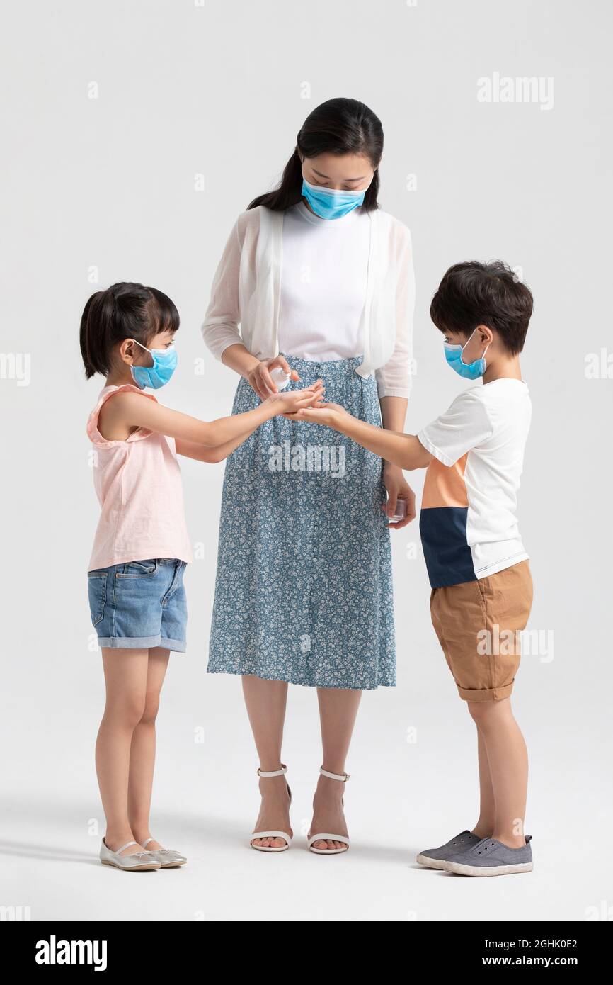 Bambini che usano l'igienizzatore per le mani con l'aiuto della madre Foto Stock