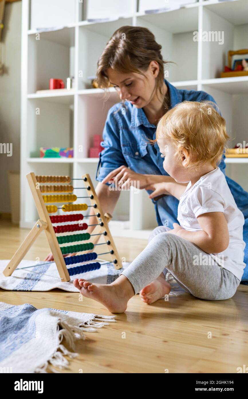 Madre insegnamento bambino piccolo contare su policolore legno di bambola ecologico abaco sul pavimento Foto Stock