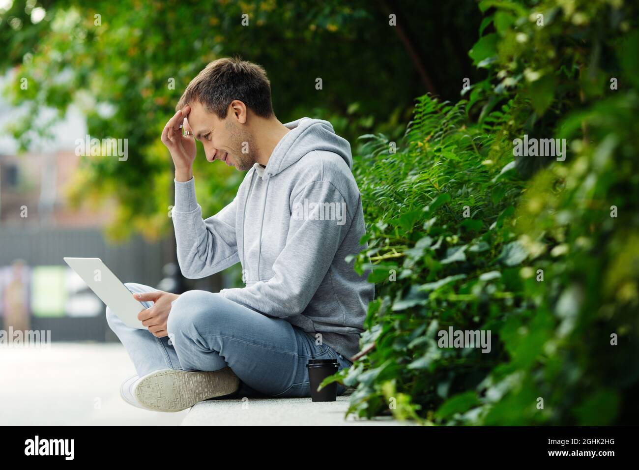 Il freelance uomo sorride i messaggi durante la chat di lavoro con i colleghi sul laptop all'esterno durante la pausa caffè Foto Stock