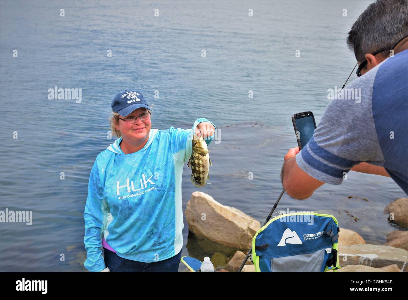 Donna in camicia sudore in una giornata fredda e palla cappuccio in vacanza con il suo pesce ha catturato all'ingresso di Morro Bay California Foto Stock
