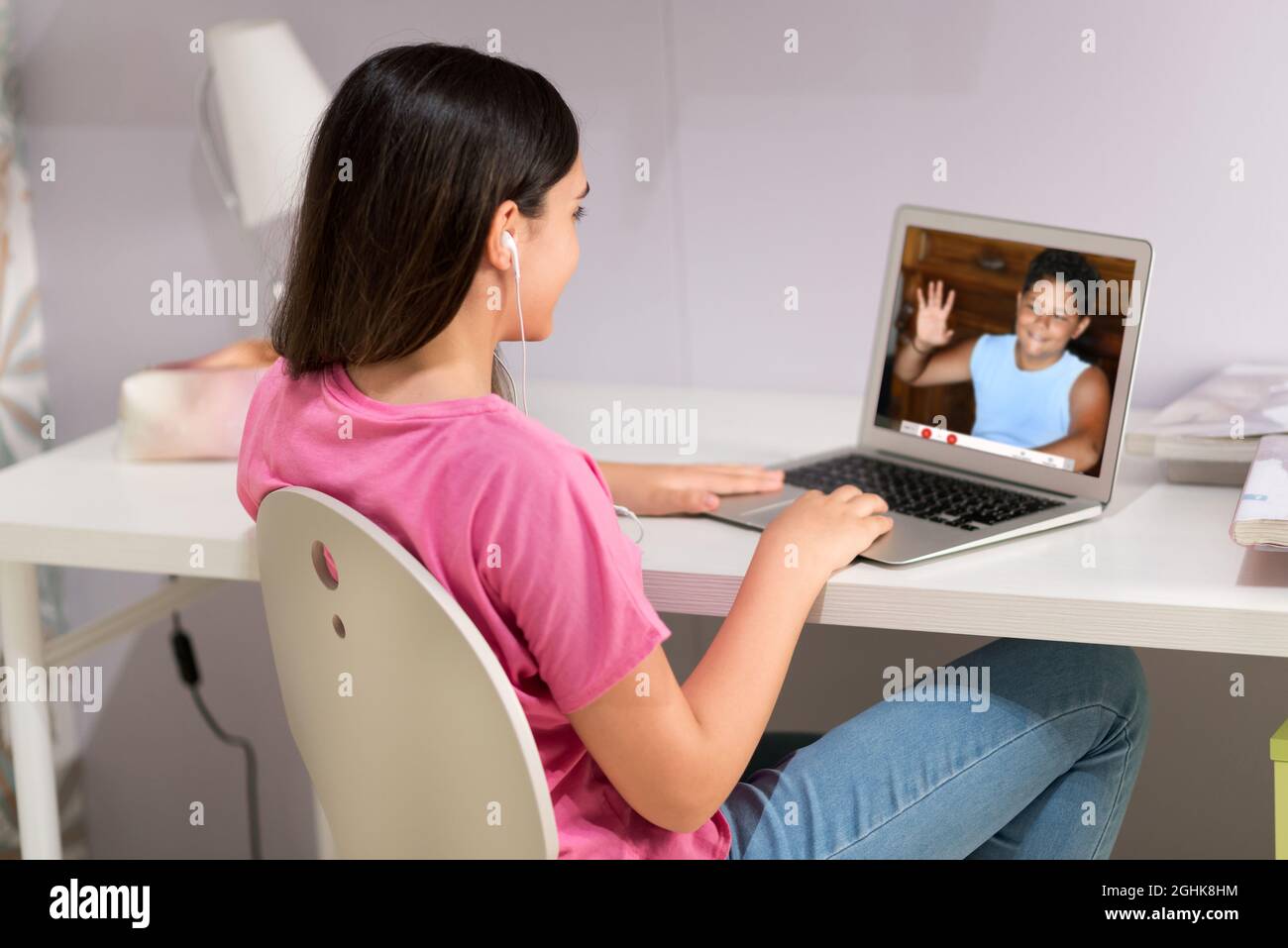 Vista laterale della ragazza adolescente in auricolari seduti al tavolo e comunicando tramite l'app di chat video sul laptop durante il periodo di social distancing a casa Foto Stock