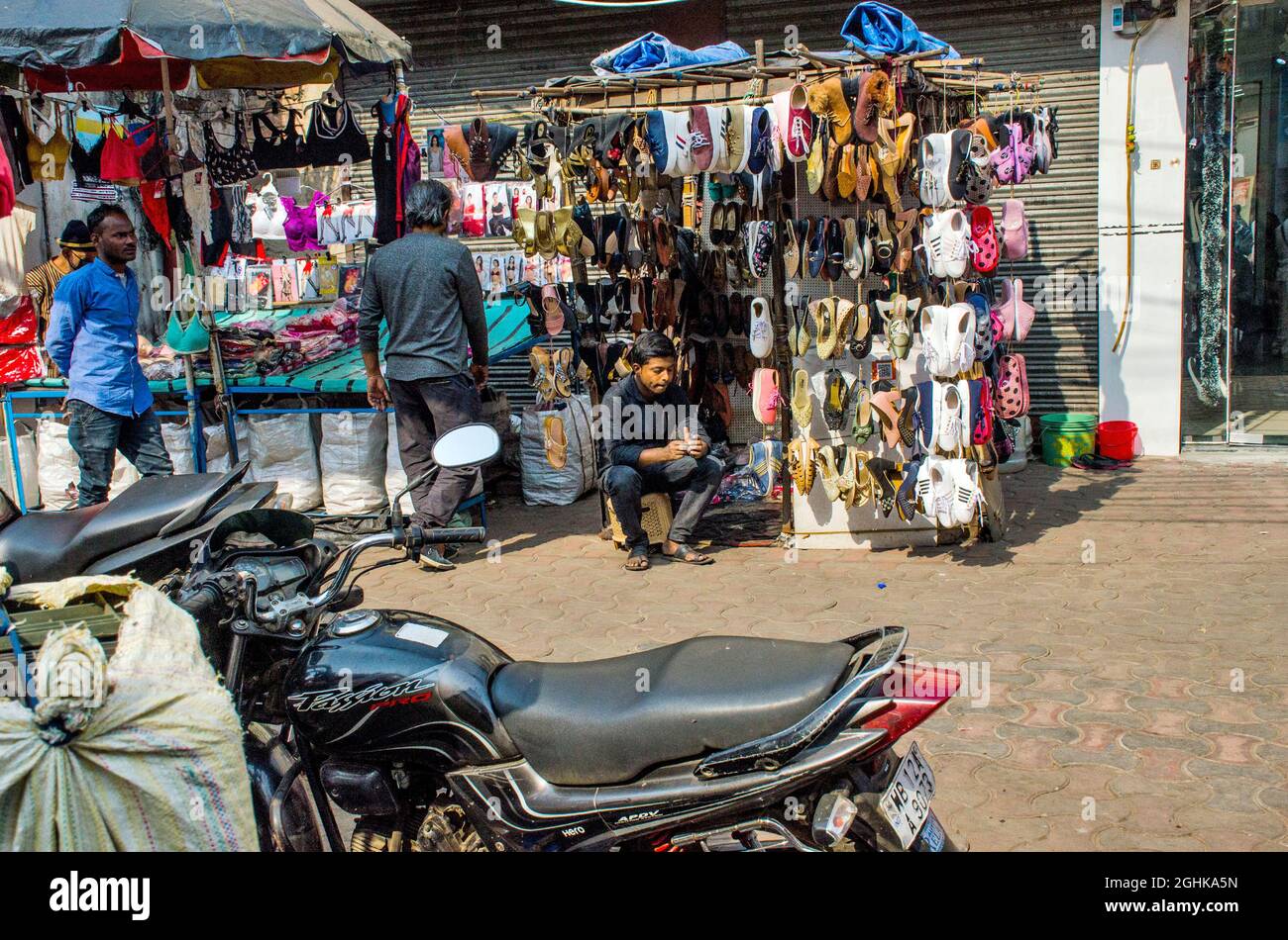 Un venditore di scarpe nella zona di Kolkata Esplanade sta aspettando un cliente organizzando il suo stock di diversi tipi di scarpe. Foto Stock