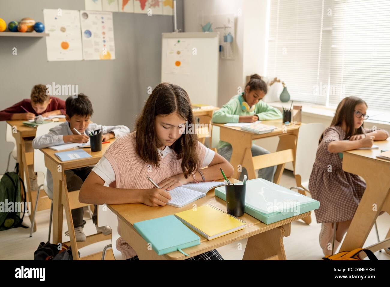 Scolgirl serio ed i suoi compagni di classe interculturali che fanno le note nei copybooks a lezione Foto Stock