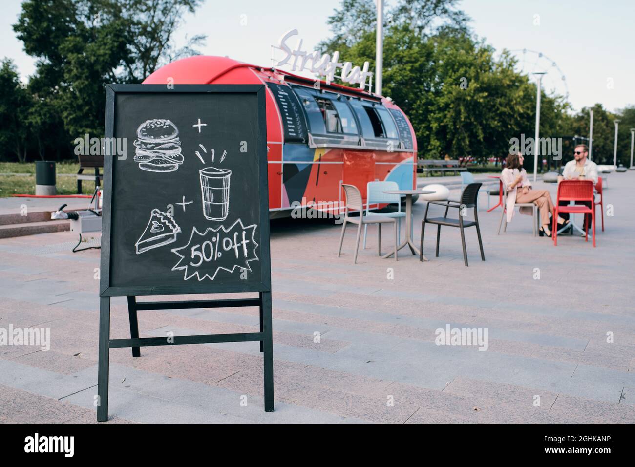 Annuncio di sconto per il cibo di strada in lavagna contro il camion alimentare in ambiente urbano Foto Stock
