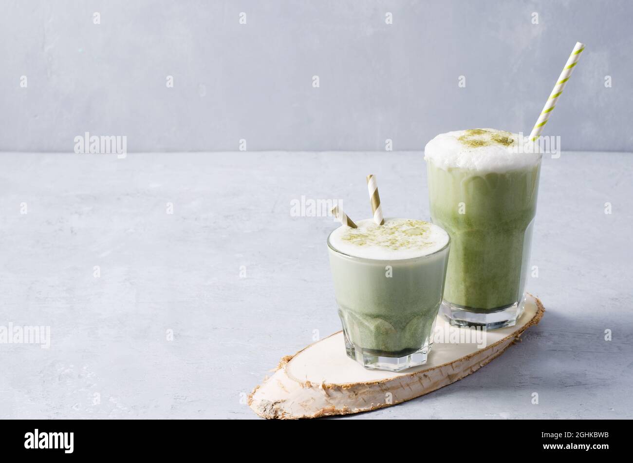 Bevete il caffè latte matcha in un bicchiere di vetro su un supporto di legno con tubi e schiuma su un fondo di cemento Foto Stock