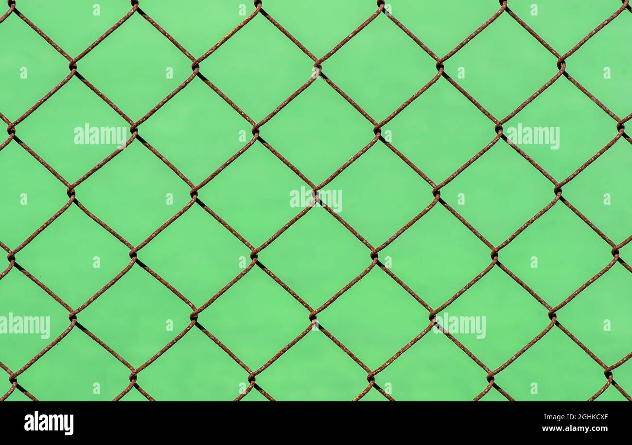 Fence di collegamento a catena arrugginita su sfondo sfocato verde, messa a fuoco poco profonda Foto Stock