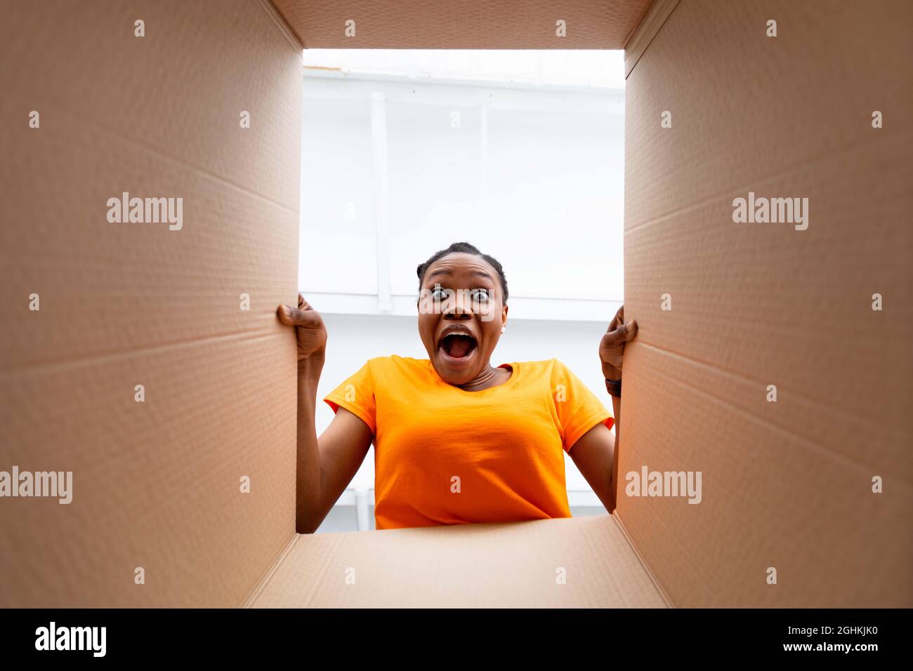 Giovane donna afroista guardando all'interno della scatola del pacco, urlando OMG in eccitazione, ottenendo l'ordine in linea all'interno, vista dal basso Foto Stock