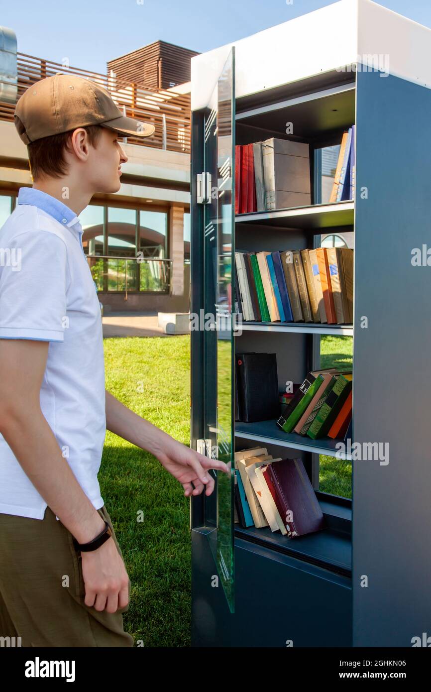 Un giovane uomo apre la porta di vetro e prende libri da un punto di scambio libri gratuito. Foto Stock