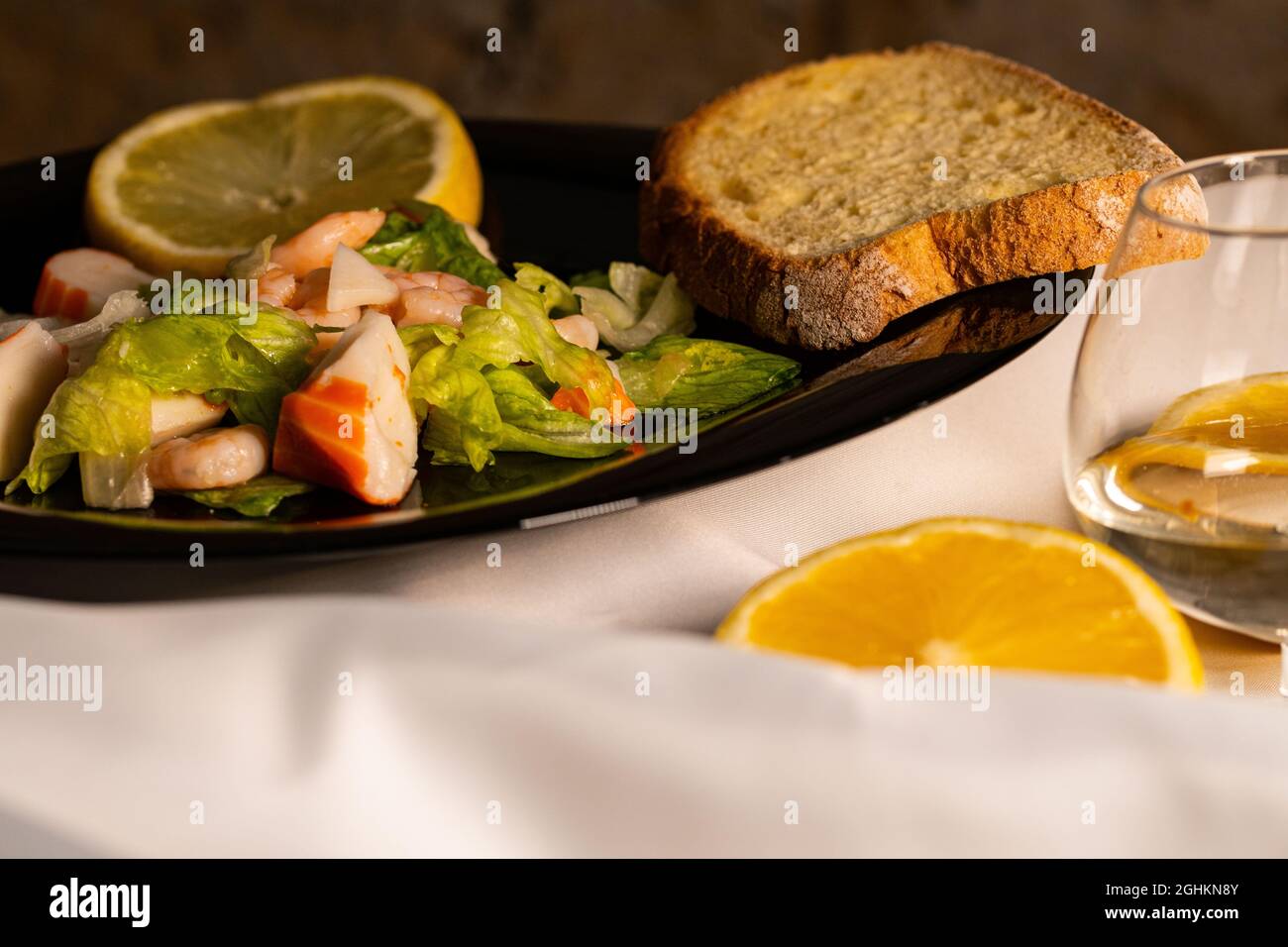 composizione di un piatto nero con gamberi e insalata di surimi su sfondo satinato bianco Foto Stock