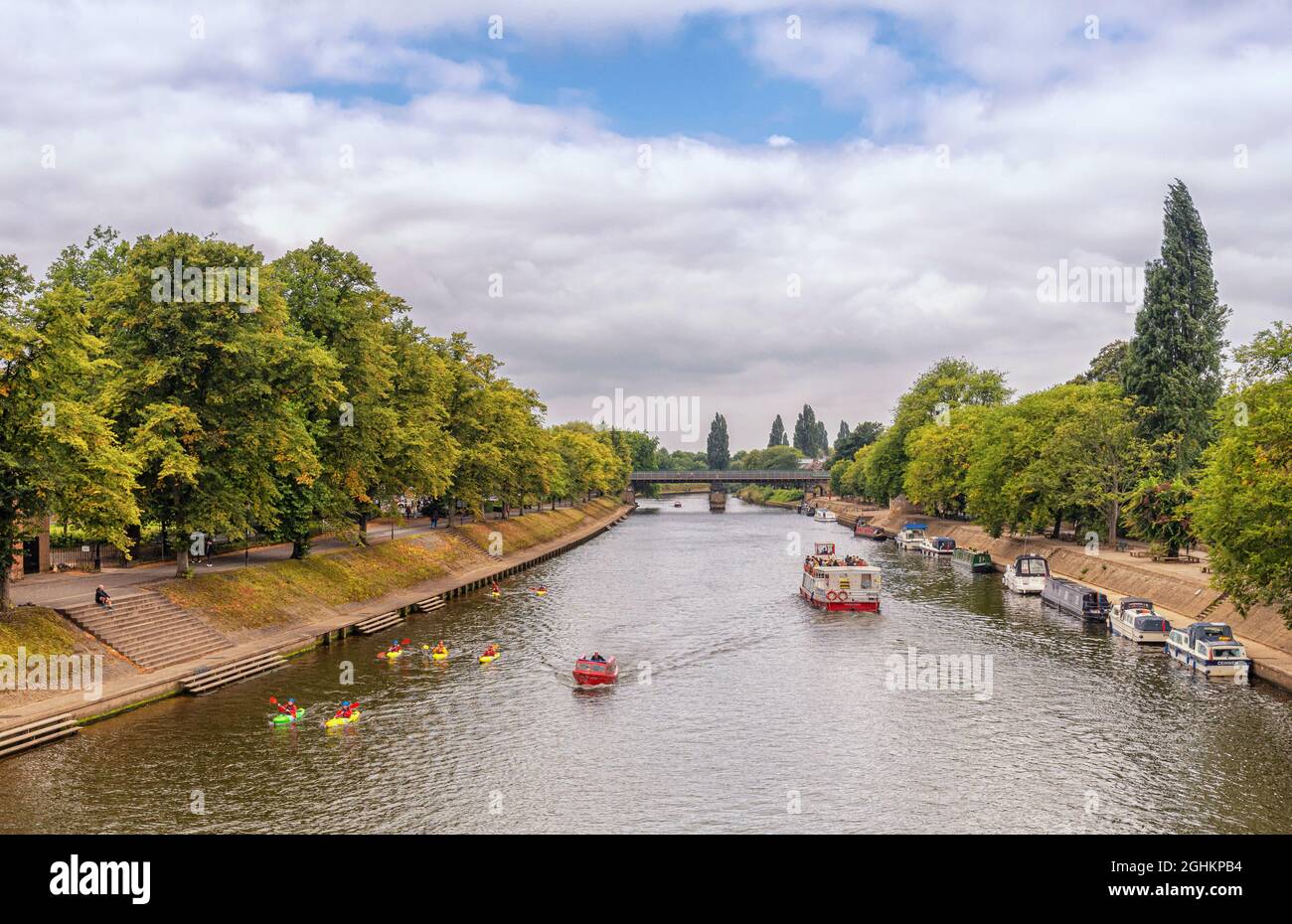 Vista lungo il fiume Ouse fino a Scarborough Bridge. Una barca da tour naviga sul fiume e una flotta di canoe pagaia nell'altra direzione accanto a una piccola barca. Foto Stock