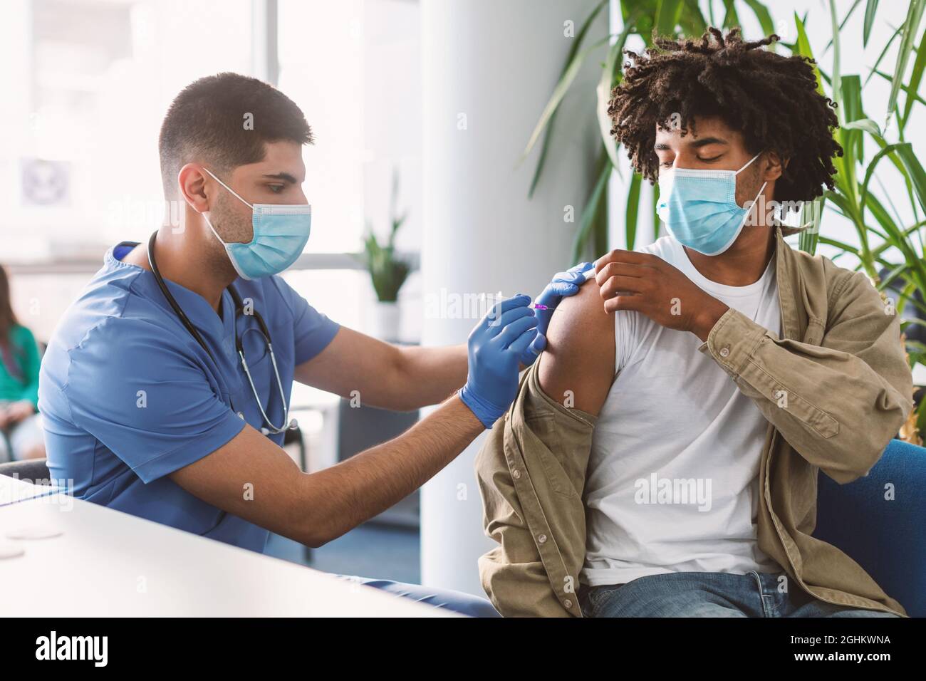 Afro Guy che riceve l'iniezione di vaccino seduto con il medico alla clinica Foto Stock