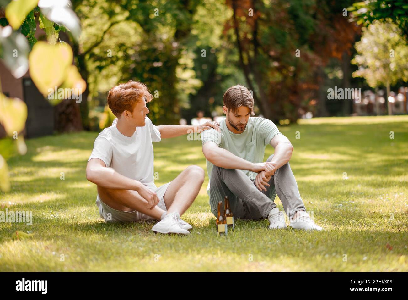 Due ragazzi con bottiglie seduti sul prato verde Foto Stock