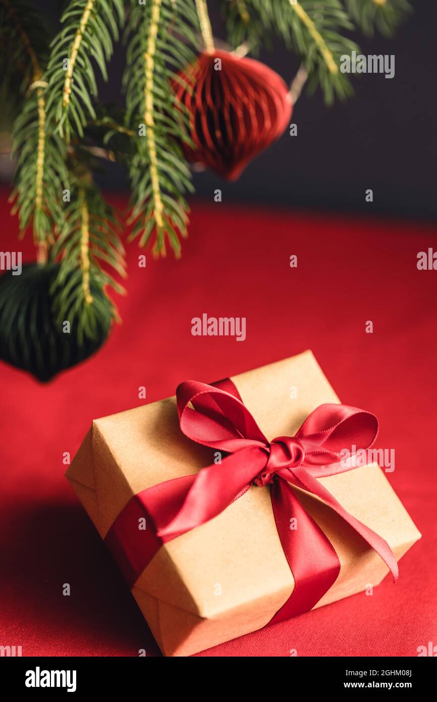 Scatola regalo di Natale su sfondo rosso sotto rami di abete. Foto Stock