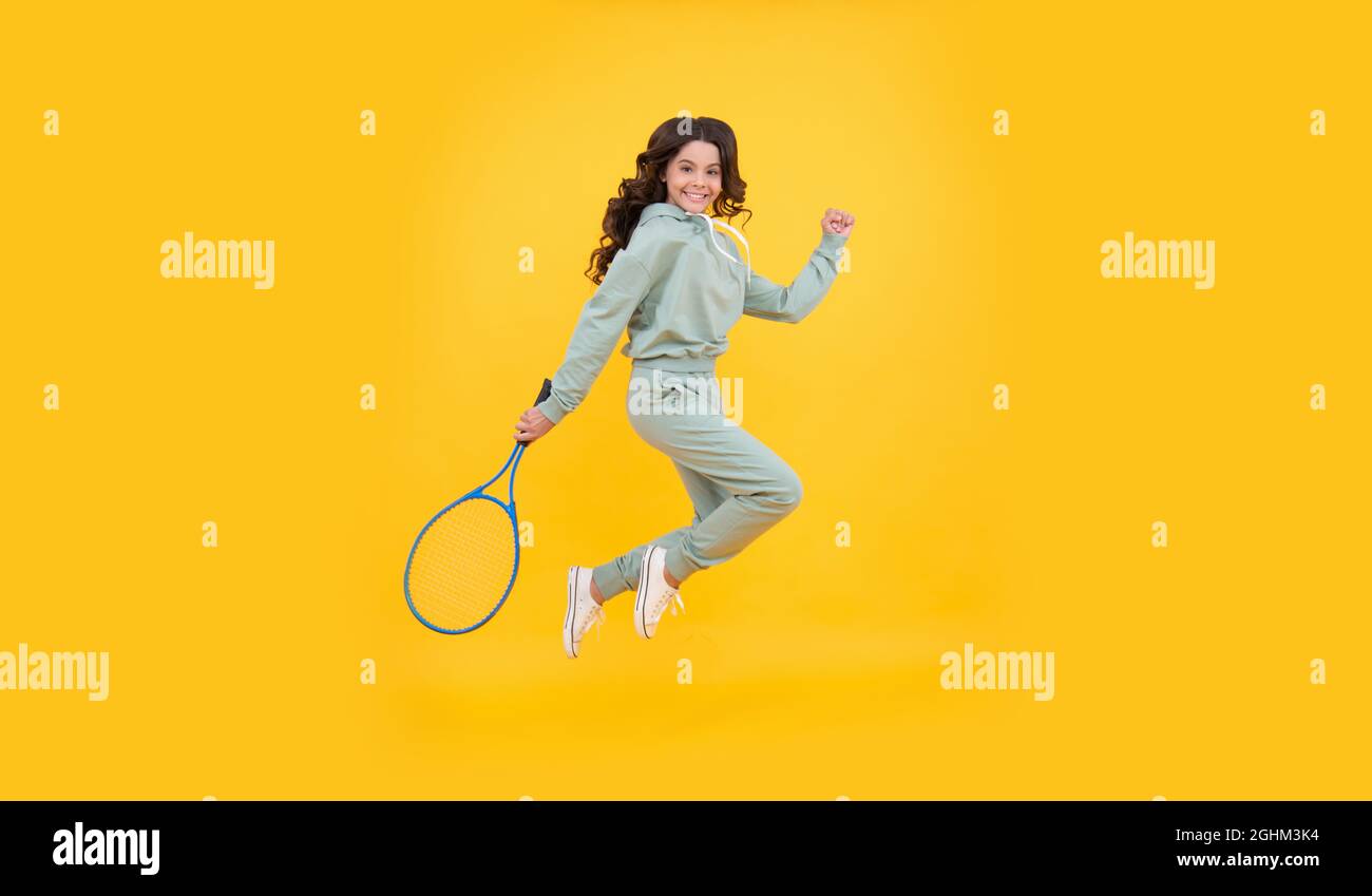 felice energico bambino salto in sportswear con racchetta da squash su sfondo giallo, successo sportivo Foto Stock