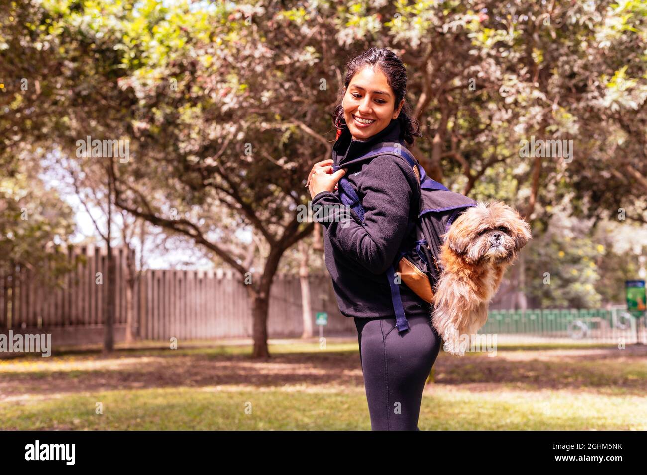 Una giovane donna affascinante cammina in natura, con uno zaino sulla spalla, da cui il suo cane sbircia fuori. Concetto di relazione e amore verso gli animali Foto Stock