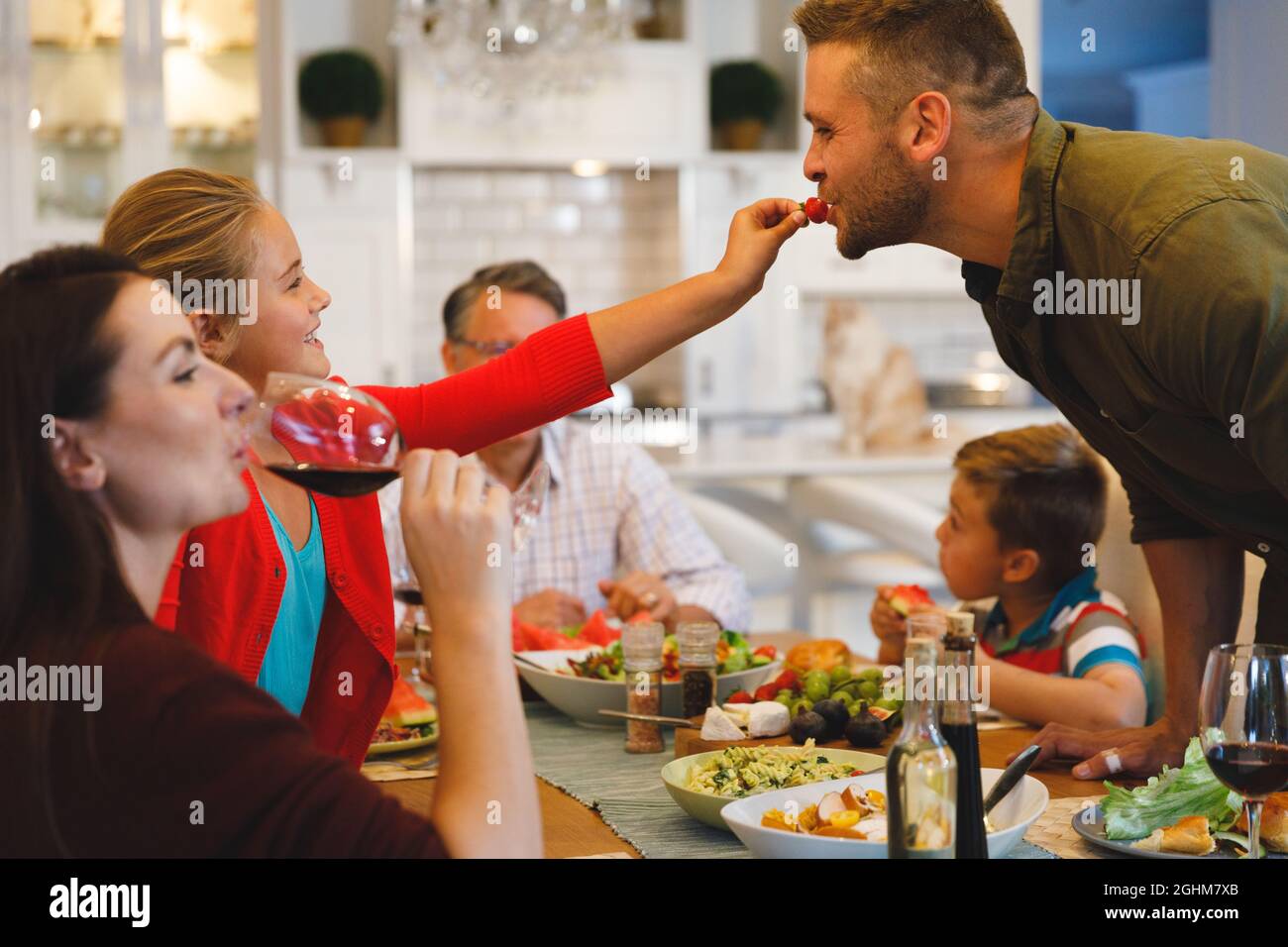 Figlia caucasica che alimenta il padre mentre si siede a tavola a cena di famiglia Foto Stock