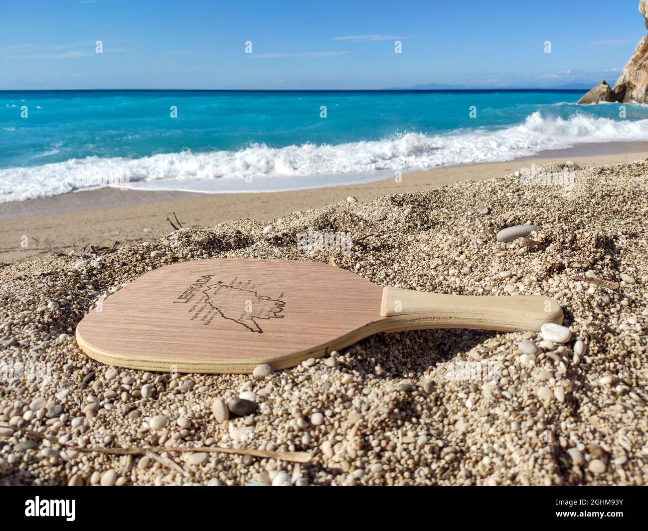 Matkot racchetta greca gioco di tennis spiaggia con mappa dell'isola di Lefkada, spiaggia di Mylos con acqua turchese e onde bianche. Attrezzatura sportiva on Foto Stock Matkot racchetta greca gioco di tennis spiaggia con mappa dell'isola di Lefkada, spiaggia di Mylos con acqua turchese e onde bianche. Attrezzatura sportiva on Foto Stock