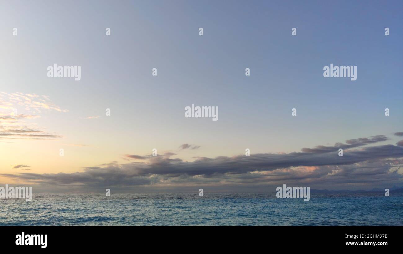 Cielo al tramonto con nuvole viola scuro sopra l'acqua di mare increspata blu. Suggestivo paesaggio nuvoloso sul mare Mediterraneo Foto Stock