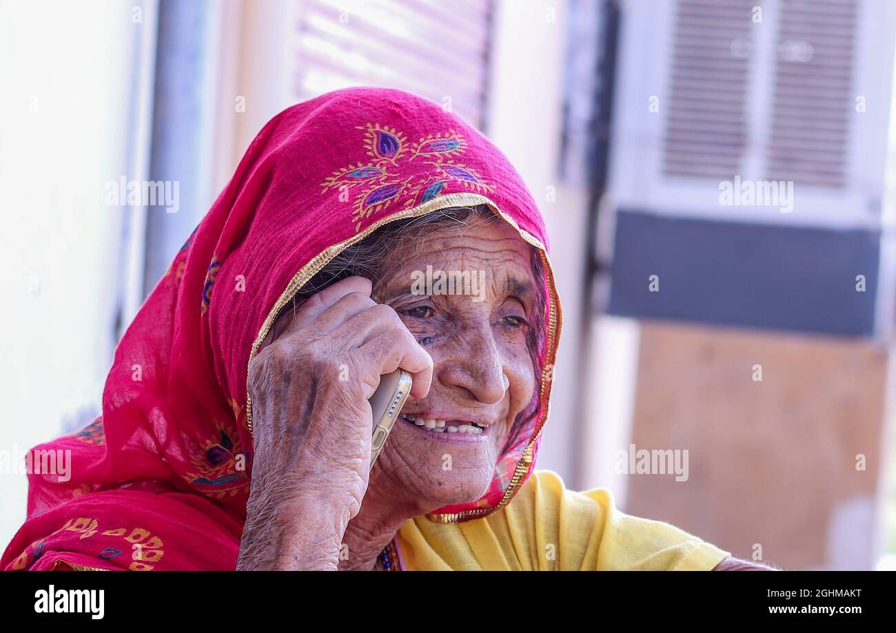 Un primo colpo di una vecchia femmina del villaggio indiano che prende una chiamata al telefono mentre sorride. Foto Stock