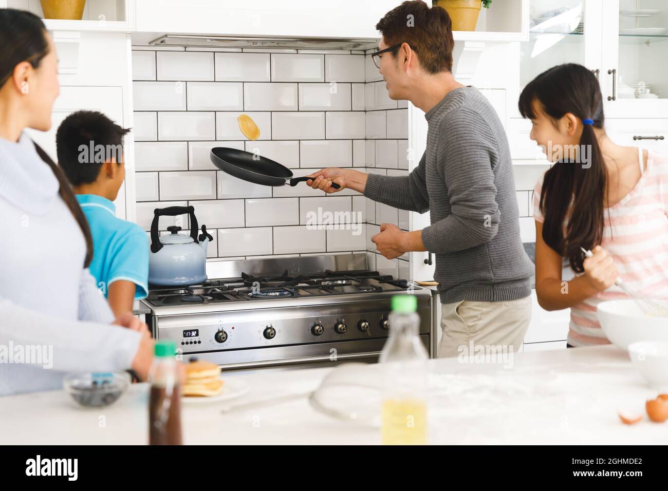 Madre asiatica, figlio e figlia che guarda il padre che lancia la frittella per la colazione in cucina Foto Stock