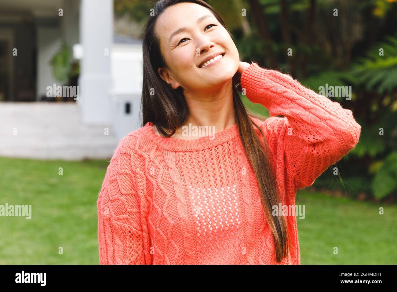 Ritratto di felice donna asiatica sorridente in giardino fuori casa famiglia indossando maglione rosa Foto Stock
