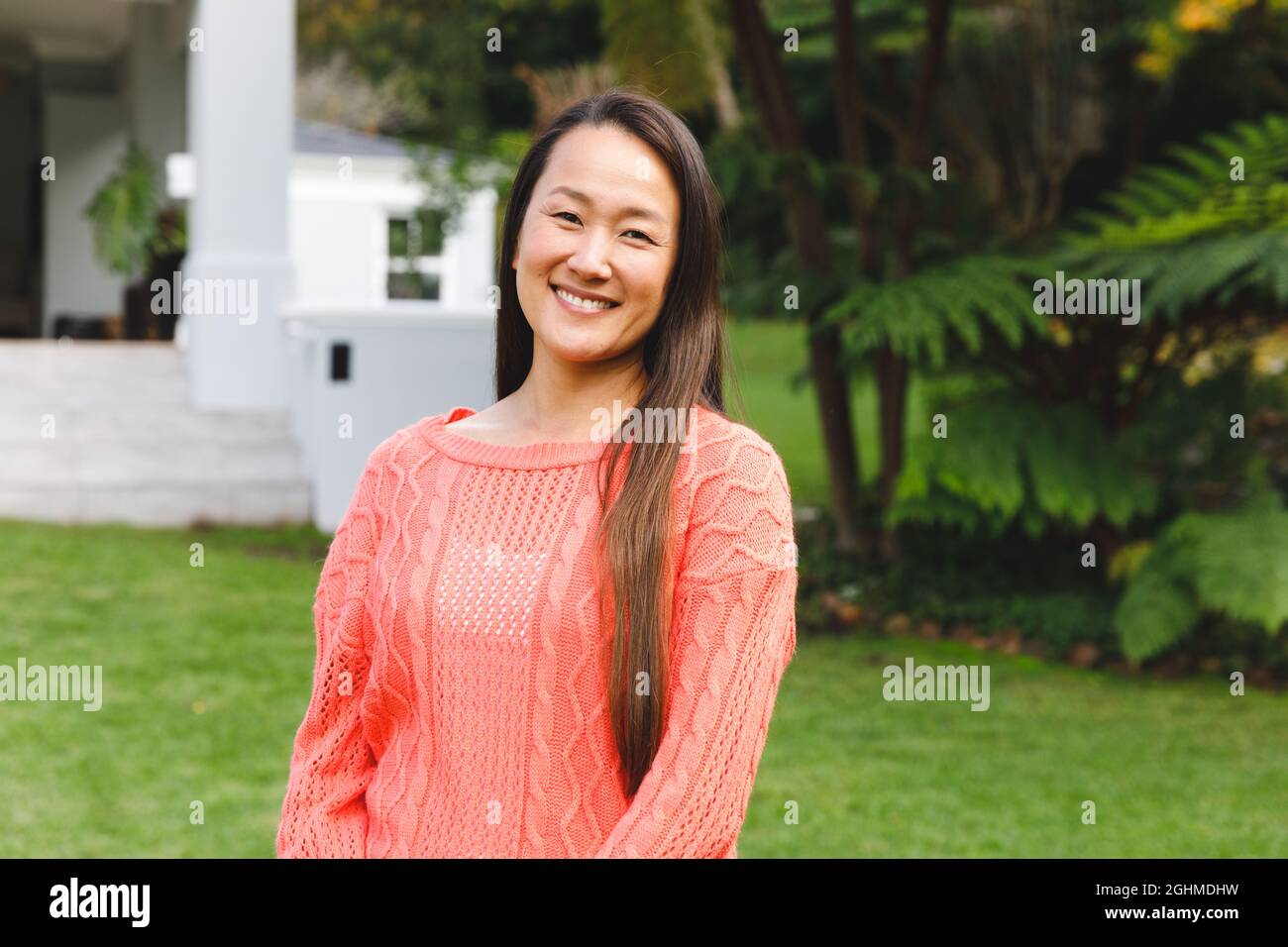 Ritratto di felice donna asiatica sorridente in giardino fuori casa famiglia indossando maglione rosa Foto Stock