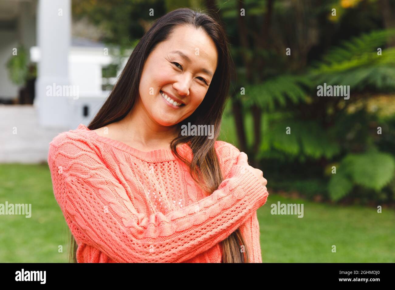 Ritratto di donna asiatica felice sorridente in giardino fuori casa famiglia indossando un maglione rosa. Godendo tempo libero da solo a casa. Foto Stock