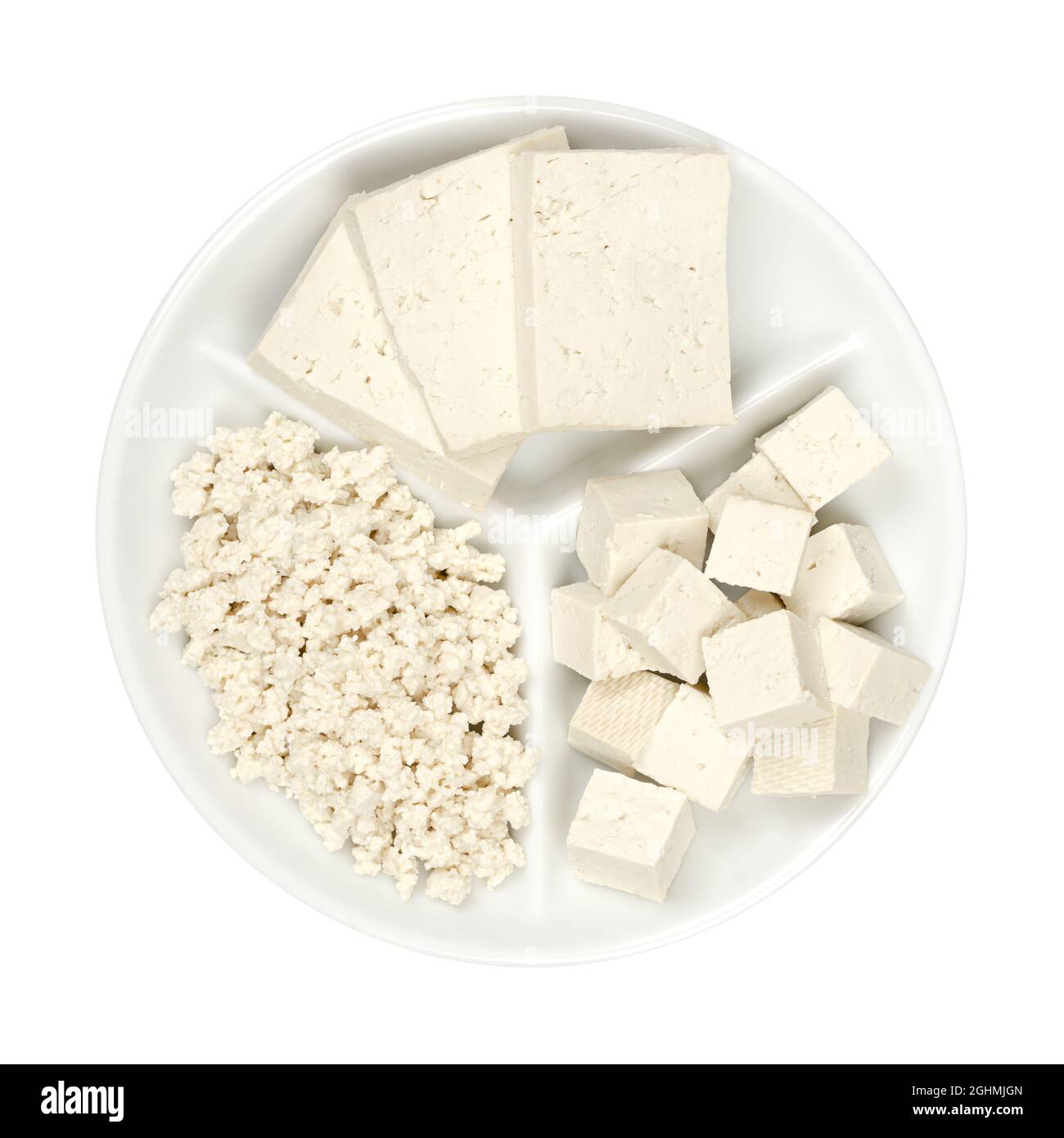 Tofu bianco lavorato, su un piccolo piatto da portata bianco. Tre fette, cubetti e tofu sbriciolato. Cagliata di fagiolo fatta di latte di soia coagulato. Foto Stock