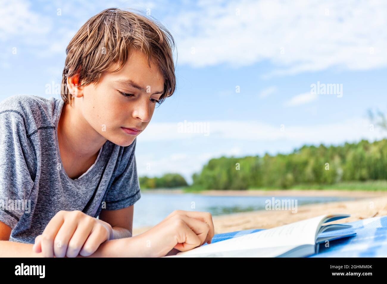 Giovane ragazzo sdraiato sulla spiaggia a Rothsee in Baviera, Germania e sta leggendo un libro con interesse Foto Stock