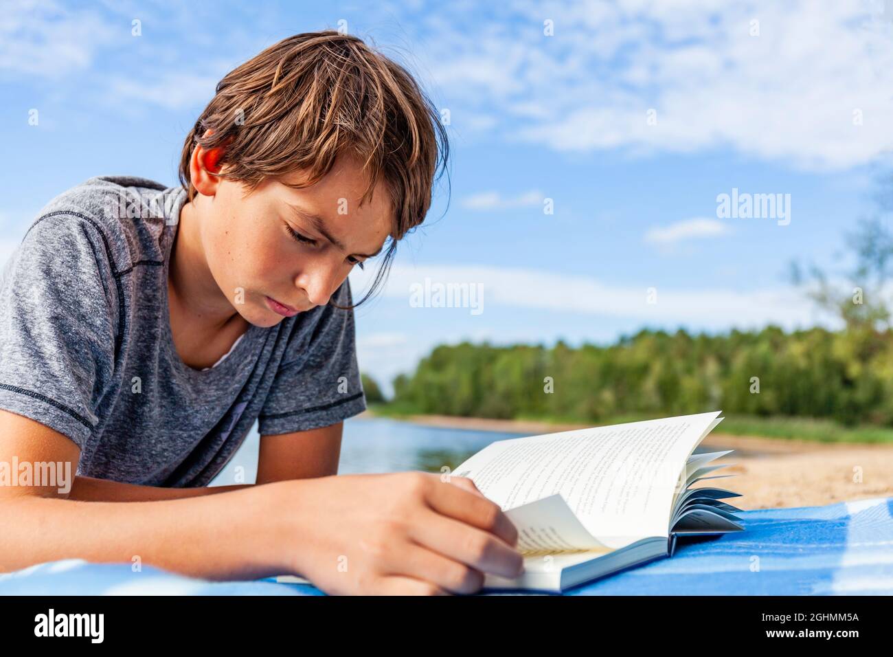 Giovane ragazzo sdraiato sulla spiaggia a Rothsee in Baviera, Germania e sta leggendo un libro con interesse Foto Stock