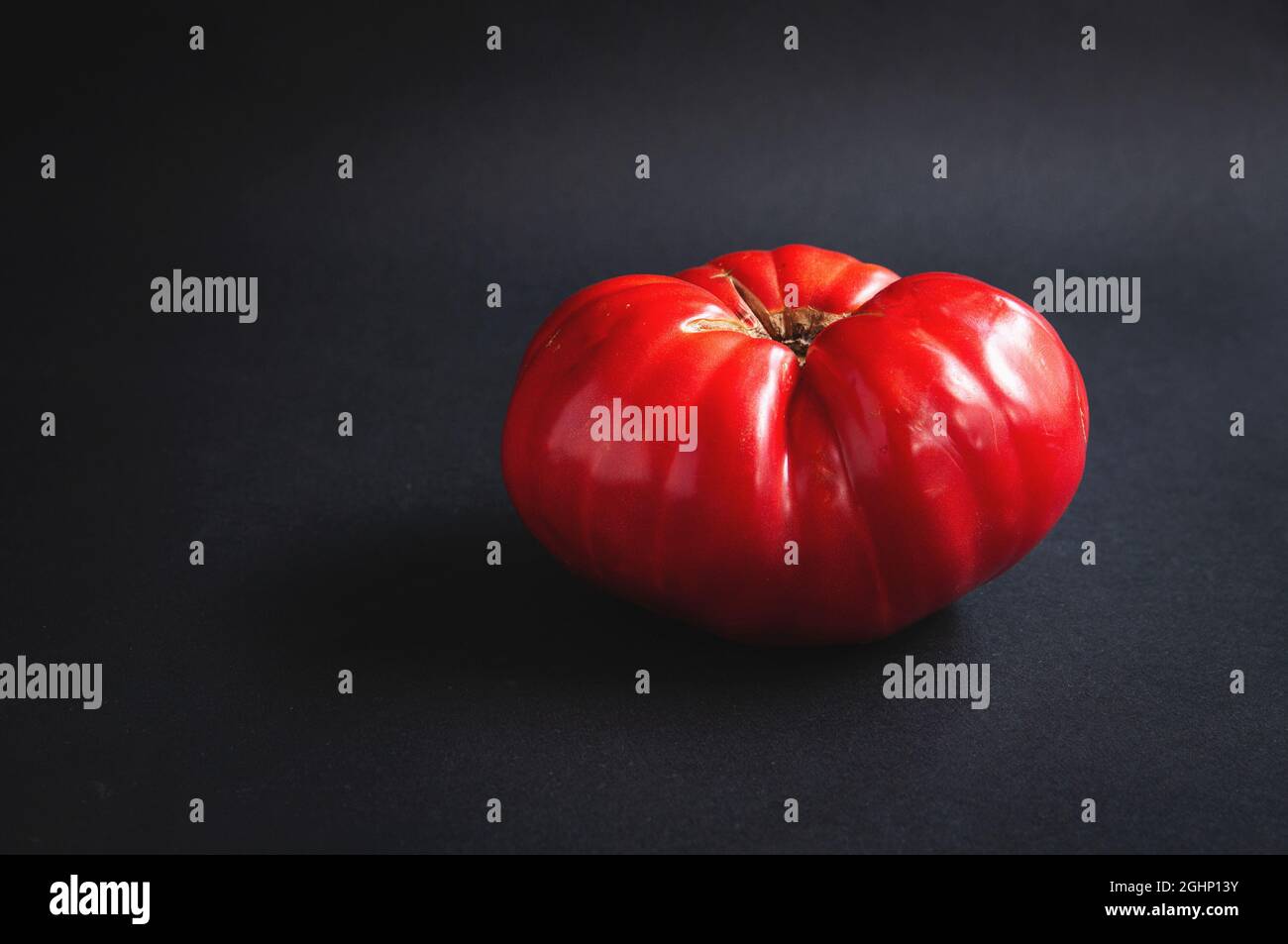 Enorme pomodoro rosso grande su una tavola nera su sfondo scuro Foto Stock