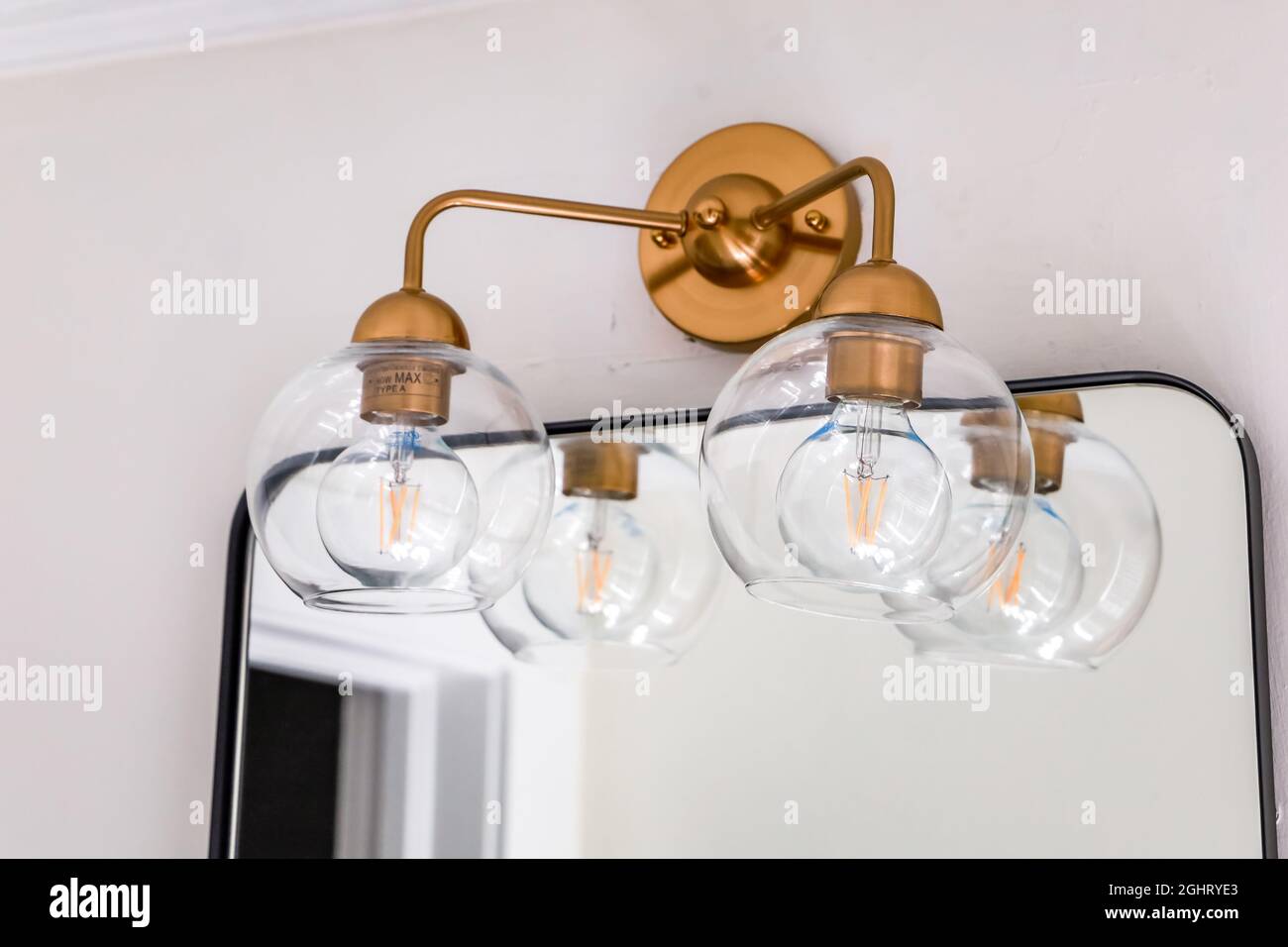 Una doppia ficture di vetro trasparente con accenti di ottone dorato in un piccolo bagno ospiti sulla parte superiore di uno specchio di stile retrò riammed nero Foto Stock