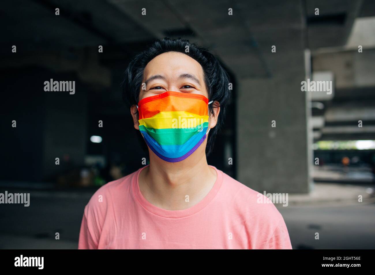 Giovane uomo asiatico felice indossando una maschera arcobaleno modellato che rappresenta il supporto LGBT e l'orgoglio durante Covid-19 o Coronavirus Foto Stock