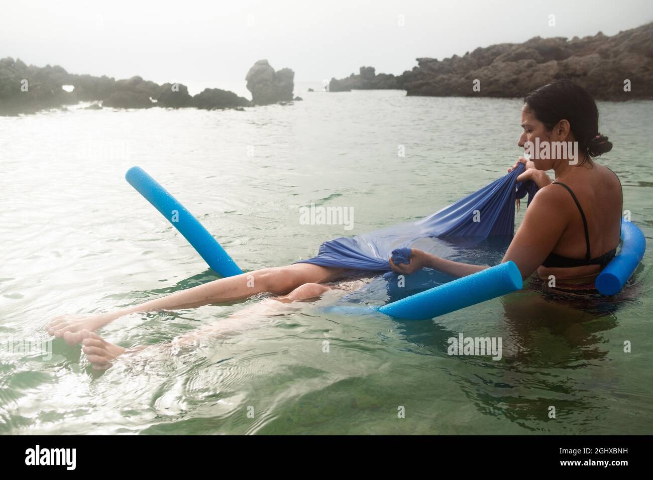 le donne galleggiano un rilassante scialle d'acqua nel mare calmo al tramonto con biliardo e scialle, una nuova tecnica curativa e rilassante Foto Stock